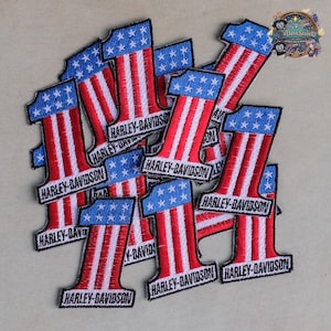 Op de afbeelding: Een verzameling geborduurde patches in de vorm van het cijfer één, met een blauw veld met witte sterren aan de bovenkant en rode en witte verticale strepen eronder. Elke patch bevat de zwarte tekst Harley-Davidson aan de onderkant.