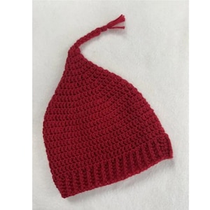 May include: A handmade, red crochet hat with a pointed top and a braided tassel. The hat is made of a textured yarn and has a ribbed brim. The hat is likely for a baby or child.