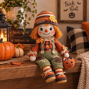 May include: A crocheted scarecrow doll with orange yarn hair, wearing a striped hat with the word stitch embroidered on it, a plaid shirt, and green overalls. The doll features a small yellow leaf on the hat and holds a small pumpkin basket.