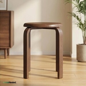 May include: A wooden stool with a round seat and curved legs. The stool is made of a dark brown wood and has a simple, modern design. The stool is placed on a light brown wooden floor.