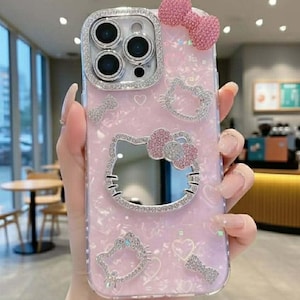 Peut inclure: Coque de t&eacute;l&eacute;phone rose avec un motif Hello Kitty. L'&eacute;tui pr&eacute;sente un n&oelig;ud scintillant, des c&oelig;urs et des ornements de visage Hello Kitty. L'objectif de la cam&eacute;ra est entour&eacute; d'un cadre argent&eacute; orn&eacute; de pierres pr&eacute;cieuses.