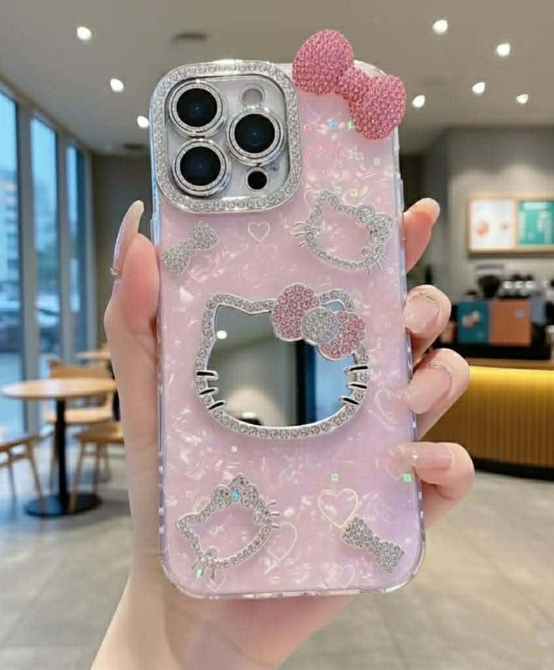 Peut inclure: Coque de t&eacute;l&eacute;phone rose avec un motif Hello Kitty. L'&eacute;tui pr&eacute;sente un n&oelig;ud scintillant, des c&oelig;urs et des ornements de visage Hello Kitty. L'objectif de la cam&eacute;ra est entour&eacute; d'un cadre argent&eacute; orn&eacute; de pierres pr&eacute;cieuses.