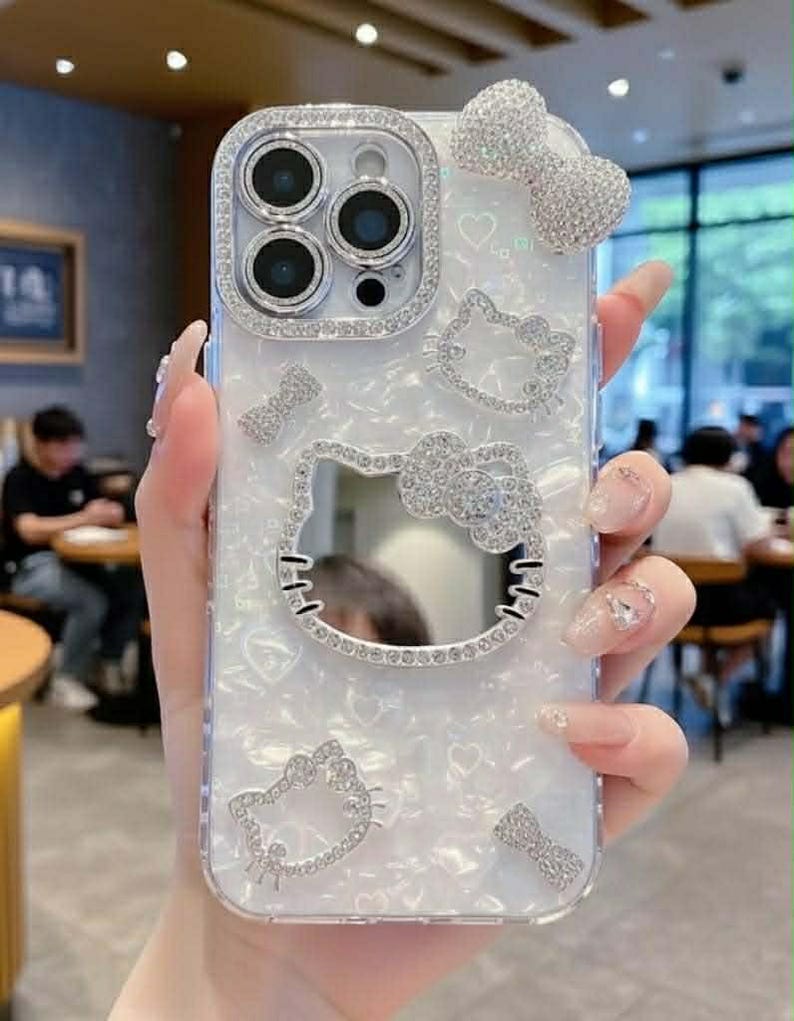 Peut inclure: Coque de t&eacute;l&eacute;phone transparente avec un fond nacr&eacute; blanc, orn&eacute;e de strass &eacute;tincelants. La coque pr&eacute;sente un motif Hello Kitty, des n&oelig;uds et des c&oelig;urs. L'objectif de l'appareil photo est entour&eacute; d'une bordure en strass.