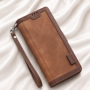 May include: A rectangular brown wallet case with a smooth, matte-textured center panel and a darker brown stitched border. The case features a detachable wrist strap attached by a silver metal clasp and a small rectangular tab on the front cover.