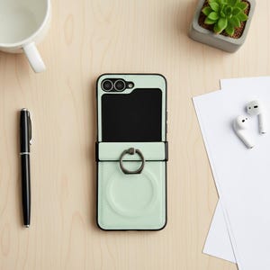 May include: A mint green phone case with a black frame and a ring holder. The case has a black interior and a card slot. A black pen, white mug, succulent plant, and wireless earbuds are also visible.