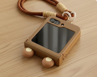 May include: A brown phone case with a matching brown strap. The case has a black screen and two small, round, light-colored accents at the bottom. The strap is made of a braided brown cord and a beige cord.