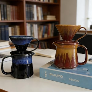 May include: Two ceramic pour-over coffee makers. One is black with blue accents, the other is brown with yellow and red accents. Both have a cone-shaped filter holder and a pitcher with a handle. The coffee makers are on a white surface.