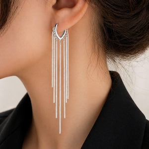 Puede incluir: Pendientes de aro plateados con múltiples barras verticales colgantes. Los pendientes son de color plateado brillante y se llevan en la oreja. El diseño es moderno y minimalista, adecuado para diversas ocasiones.