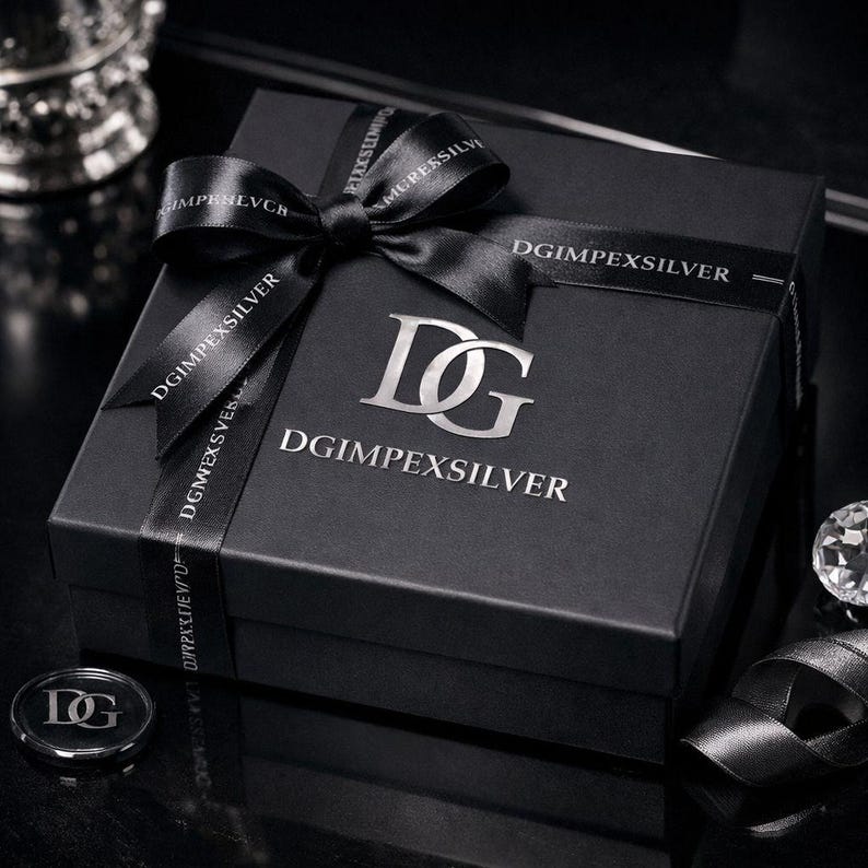 May include: A black gift box with a silver logo and the text "DGIMPEXSILVER" on the box and ribbon. The box is tied with a black ribbon and bow. A small silver coin with the logo is also visible.