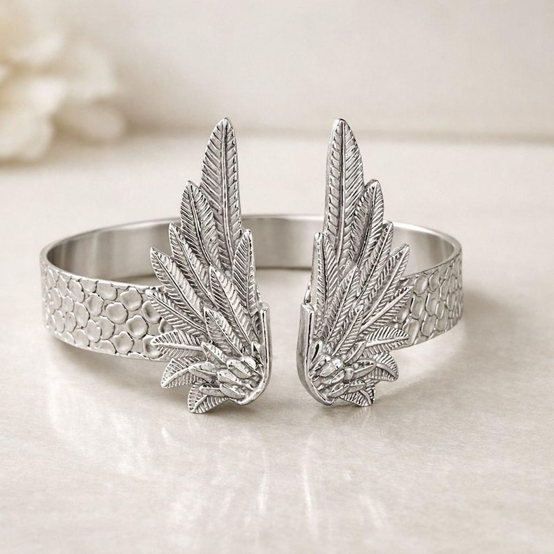 May include: Silver-toned cuff bracelet featuring a detailed feather wing design on each end. The bracelet has a textured band with a honeycomb pattern. A stylish accessory for everyday wear.