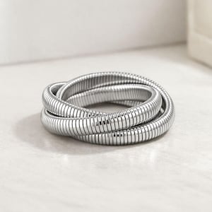 以下が含まれることがあります： 銀色の、柔軟なブレスレット。コイル状のデザイン。ブレスレットは、複数の接続された円筒形のセグメントでできており、テクスチャ加工されたヘビのような外観を作り出しています。白い表面に表示されています。