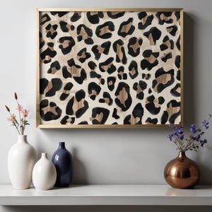 May include: A framed artwork featuring a leopard print design in black, brown, and beige. The artwork is in a gold frame and is displayed above a white shelf with vases and flowers.