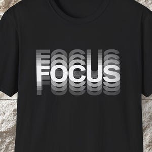 May include: Black crew neck t-shirt with the word "FOCUS" in white, stacked and slightly offset to create a layered effect. The shirt is made of a soft material and is suitable for casual wear.
