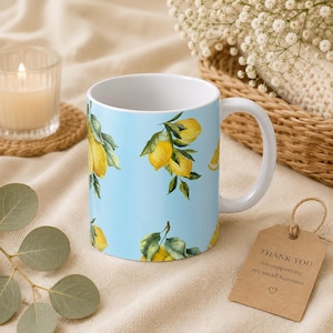 May include: A ceramic mug with a light blue background featuring a repeating pattern of yellow lemons with green leaves. The mug has a white interior and a curved handle. A brown paper tag with the text THANK YOU for supporting my small business.