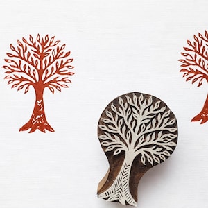 Könnte beinhalten: Ein Holzblock mit einem geschnitzten Baumdesign, neben zwei rotbraunen Baumdrucken. Die Baumdrucke und der Block befinden sich auf weißem Hintergrund. Der Block hat einen Griff.