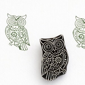 May include: A black and white owl stamp with detailed floral and dot patterns, with two green owl prints. The stamp is a tool for creating owl designs, ideal for crafting or art projects. The image is on a white background.