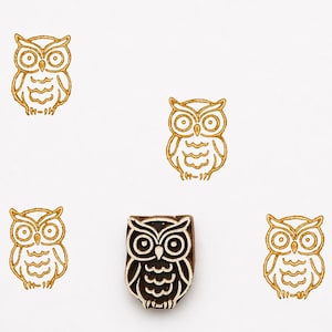 May include: An image showing owl-themed stamps and prints. There are six owl designs: five gold outline prints and one dark brown wooden stamp. The owls have large eyes and detailed feather patterns, ideal for crafting and scrapbooking projects.