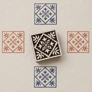 May include: A wooden block stamp with a detailed floral design, surrounded by four square patterns in blue and rust colours. The patterns feature a central floral motif within a diamond-shaped border, ideal for crafting and decorative projects.