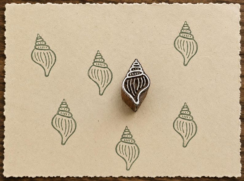 Hand-carved Whelk Shell wooden printing block with sage green shell impressions on textured handmade cream paper.