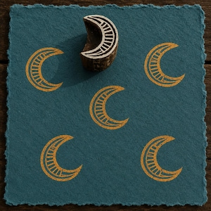 May include: A dark teal square paper with a deckled edge featuring five stamped golden crescent moon designs. A single wooden crescent moon stamp is positioned at the top centre, showing a carved interior pattern of parallel lines.