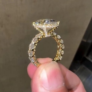 May include: A gold ring featuring a large, oval-cut center stone surrounded by a halo of small, round-cut diamonds. The band is encrusted with a continuous row of round-cut diamonds, creating a sparkling, multi-faceted appearance throughout the entire piece.
