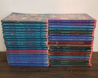 May include: A stack of 28 paperback books with blue and red covers. The books are all part of the "The Baby-Sitters Club" series. The titles of the books are visible on the spines. The books are arranged in two stacks, one on top of the other.