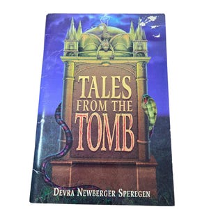 Puede incluir: Un libro titulado "Tales From The Tomb" con una ilustración de lápida. La portada presenta un diseño de lápida con un murciélago, una serpiente y el nombre del autor, Devra Newberger Speregen.