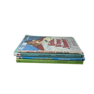 Puede incluir: Una pila de cuatro libros de bolsillo de Marilyn Sachs. Los títulos incluyen "Hello Wrong Number", "Amy and Laura", "A Secret Friend" y "The Truth About Mary Rose". Los libros son de varios colores, con el libro superior que presenta a una mujer en la portada.
