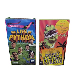 Puede incluir: Dos cintas VHS vintage. La primera, "The Life of Python", presenta un cielo azul y un campo verde con las caras del elenco. La segunda, "Monty Python's Flying Circus", tiene un gráfico de monstruo verde sobre un fondo rojo.