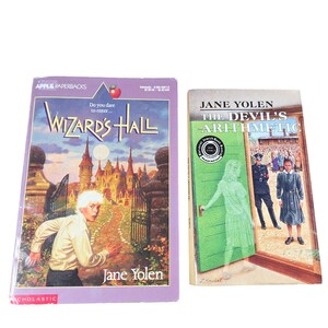 May include: Two paperback books. The first, "Wizard's Hall" by Jane Yolen, features a boy running toward a castle on a purple cover. The second, "The Devil's Arithmetic" by Jane Yolen, shows a girl in a green doorway.