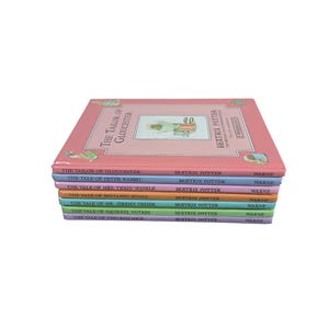 Op de afbeelding: Een stapel kinderboeken van Beatrix Potter, waaronder "The Tailor of Gloucester" en "The Tale of Peter Rabbit". De boeken hebben kleurrijke covers in roze, blauw, groen en geel.