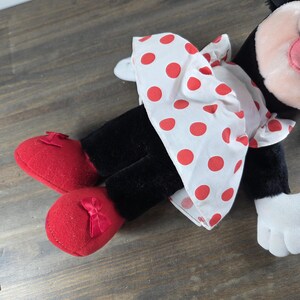 Pu&ograve; includere: Una bambola di peluche di Minnie Mouse, con un vestito bianco a pois rossi, scarpe rosse con fiocchi e gambe nere. La bambola ha un naso rosa, guanti bianchi e orecchie nere. Un classico giocattolo per bambini.