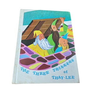 May include: Vintage children's book titled "The Three Thinkers of Thay-Lee." The cover features an illustration of three cartoon gnomes with colorful hats and clothing. The background includes a wooden structure and a patterned floor.