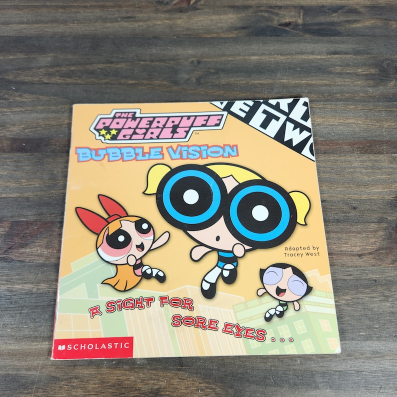 May include: A yellow book cover with the title "The Powerpuff Girls Bubble Vision: A Sight for Sore Eyes..."  The cover features the Powerpuff Girls characters, Bubbles, Buttercup, and Blossom. The book is published by Scholastic.