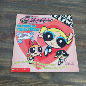 May include: A pink and red book cover with the title "The Powerpuff Girls: Bubble Trouble" and a picture of the three Powerpuff Girls. The book is based on the cartoon TV show and is published by Scholastic.