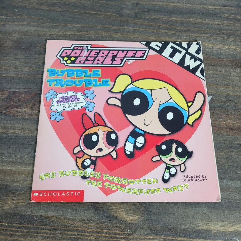 May include: A pink and red book cover with the title "The Powerpuff Girls: Bubble Trouble" and a picture of the three Powerpuff Girls. The book is based on the cartoon TV show and is published by Scholastic.