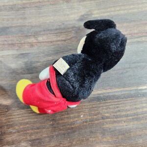 May include: Black and red plush Mickey Mouse toy with a white tag that reads "Made in China, All New Material, Polyester Fiber Fill, Surface Washable, Disney, &copy; Disney",  and "Manufactured for Disney Stores, Inc. Glendale, CA 91209".