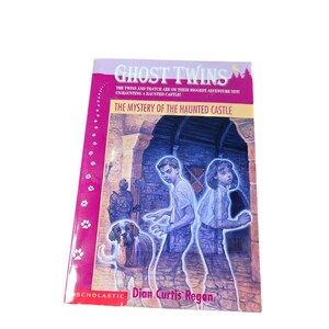 May include: A paperback book titled "Ghost Twins: The Mystery of the Haunted Castle" by Dian Curtis Regan. The cover features two children, a dog, and a castle illustration. The book has a pink spine with paw prints.