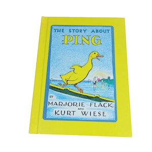 May include: A hardcover book titled The Story About Ping by Marjorie Flack and Kurt Wiese. The cover is bright yellow with a central illustration of a yellow duck standing on a green boat against a blue water background with a sunset.