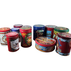 May include: Assortment of holiday themed tin cans with various designs and colours. The cans feature images of reindeer, Santa Claus, and other festive characters. The cans are all different sizes and shapes.