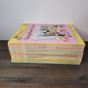 May include: A stack of 12 colourful paperback books featuring Mickey Mouse and other Disney characters. The books are titled "Young Readers Guide", "Donald and the Frog", "Mickey and the Troll", "Goofy Goes to the Fair", "Scrooge's Silly Day", "Pluto and the Big Race", "Donald's Magic Stone", "Our Wonderful Earth", "Tigger and the Apple Tree", "Mickey's Magic Bottle", and "Scrooge and the Golden Eggs". Each book has a Bantam Books logo.