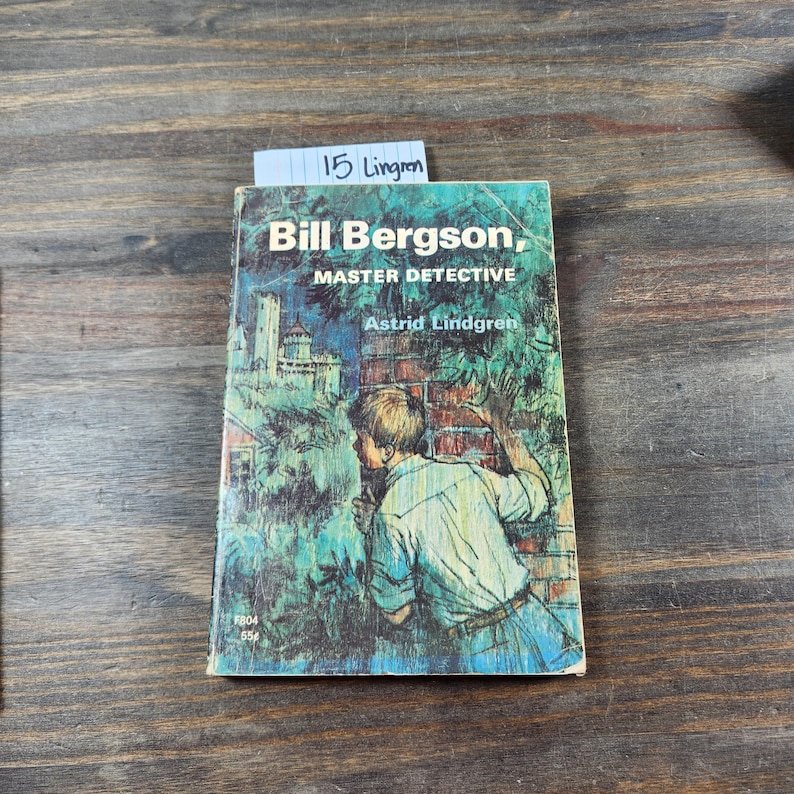 Puede incluir: Un libro de bolsillo vintage titulado "Bill Bergson, maestro detective" de Astrid Lindgren. La portada presenta una ilustraci&oacute;n de un ni&ntilde;o peque&ntilde;o mirando por encima de un muro de ladrillos.