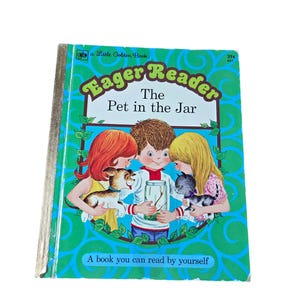 May include: A vintage children's book titled "Eager Reader: The Pet in the Jar." The cover features illustrations of three children with a puppy and a kitten. The book has a green background with a gold spine.