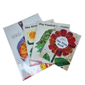 May include: A stack of children's books with colorful illustrations. The titles include "The Tiny Seed," "The Foolish Tortoise," and "The Greedy Sun." The books are by Eric Carle and published by Scholastic.