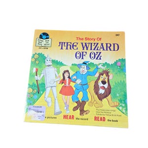 May include: A vintage children's book titled "The Story of The Wizard of Oz." The cover features illustrations of the Tin Man, Dorothy, the Scarecrow, and the Cowardly Lion. The book includes a record and is marked with a Goodwill sticker.