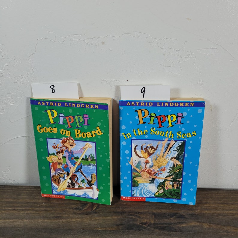 Puede incluir: Dos libros de bolsillo para ni&ntilde;os con portadas coloridas que presentan ilustraciones de Pippi Calzaslargas. El libro de la izquierda se titula "Pippi Goes on Board" y el libro de la derecha se titula "Pippi in the South Seas".