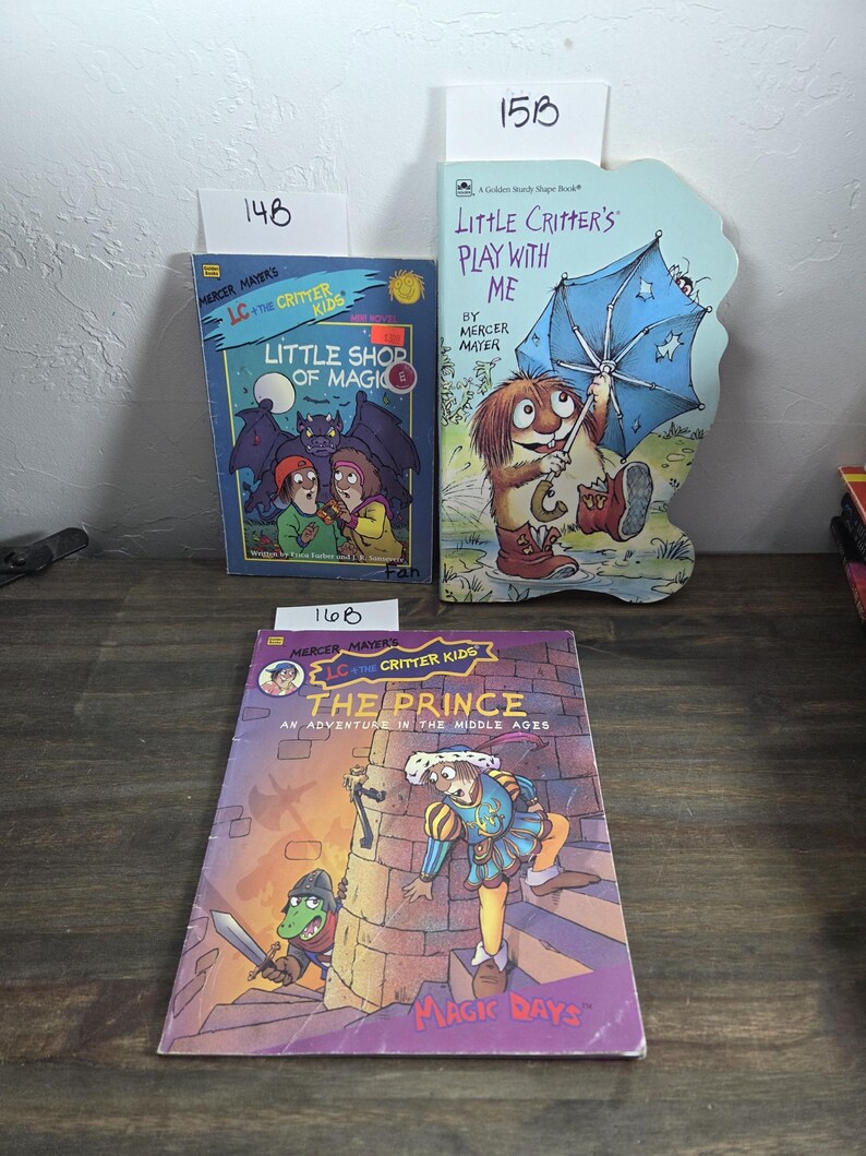 May include: Three children's books by Mercer Mayer. Titles include "Little Shop of Magic", "Little Critter's Play With Me", and "The Prince: An Adventure in the Middle Ages". The books feature colorful illustrations and are set on a wooden surface.