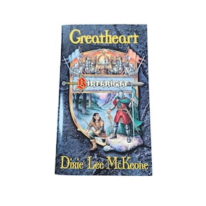 May include: A book cover with a blue background and a gold shield featuring a knight and a bowman. The title of the book is "Greatheart" and the author is "Dixie Lee McKeone".