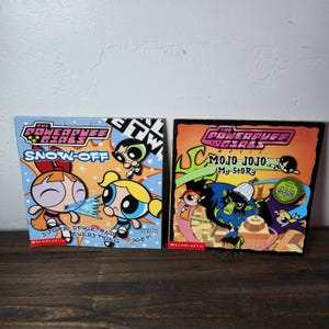 May include: Two paperback books featuring the Powerpuff Girls. The book on the left is titled "Snow-Off" and features the Powerpuff Girls in a snowy scene. The book on the right is titled "Mojo Jojo: My Story" and features Mojo Jojo, the Powerpuff Girls' nemesis, in a city scene.