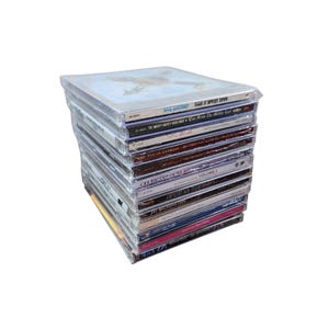 Puede incluir: Una pila de CDs en estuches de plástico transparente. La funda superior del CD tiene una imagen azul y blanca de un avión. Los títulos visibles incluyen "Spin Doctors", "The Mighty Mighty Bosstones" y "Aretha Franklin".